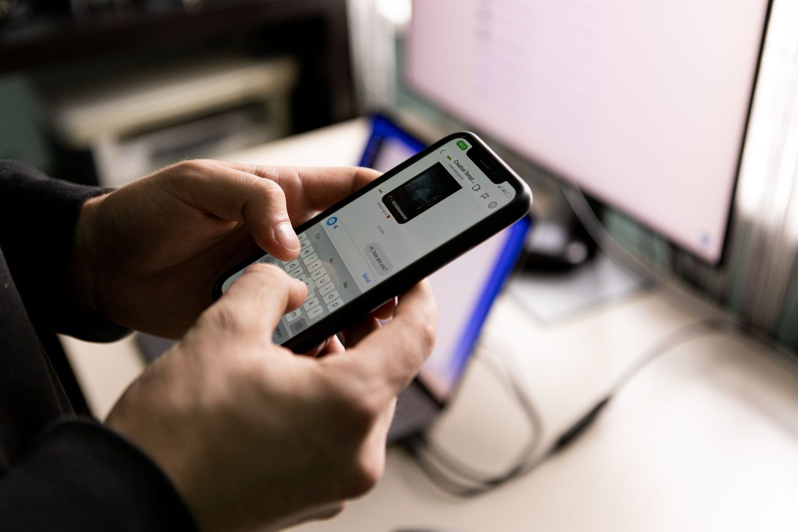 Pessoa respondendo mensagem de cliente no smartphone ao lado do computador