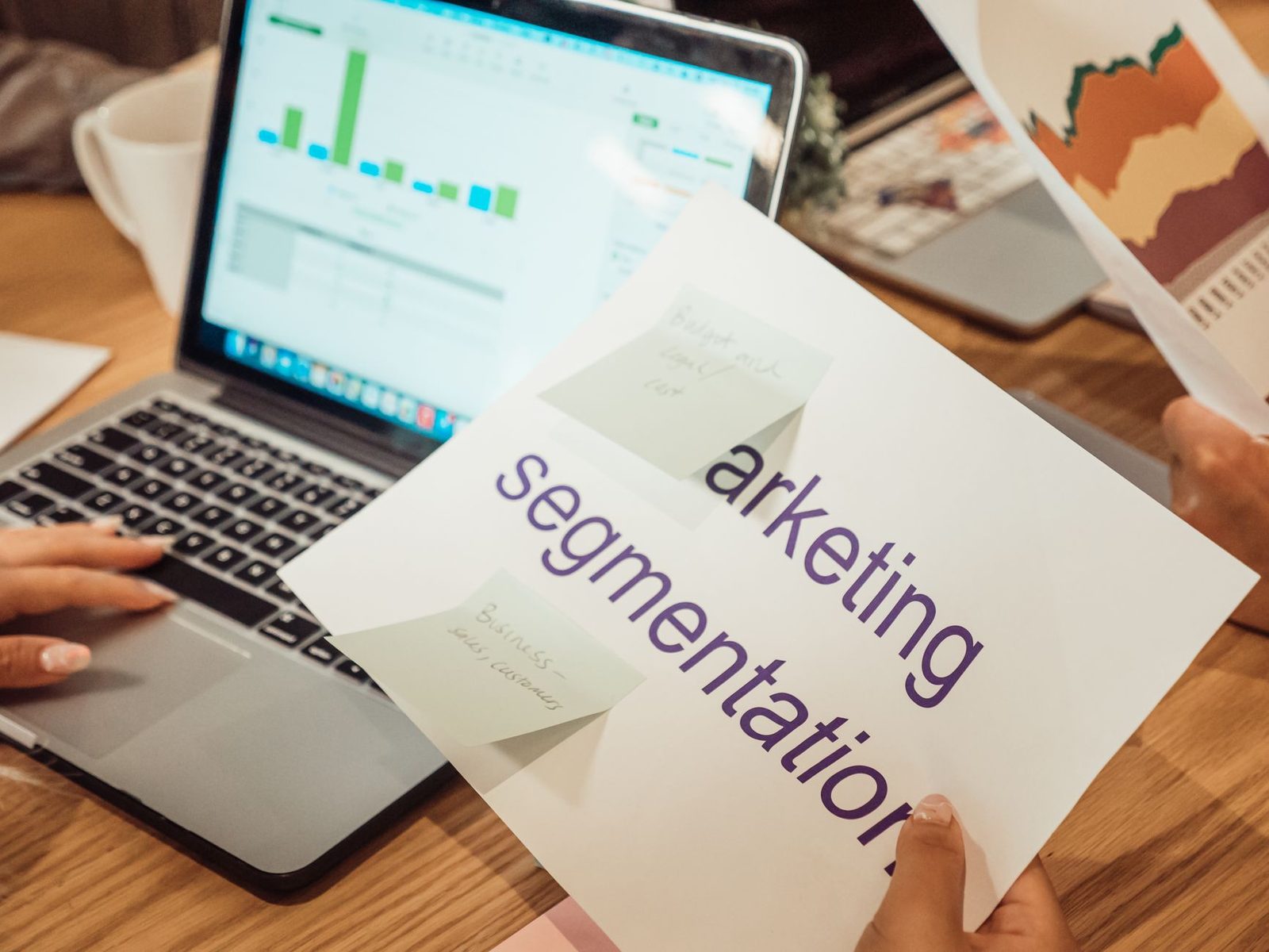 Mãos analisando dados de marketing no notebook e em relatórios impressos