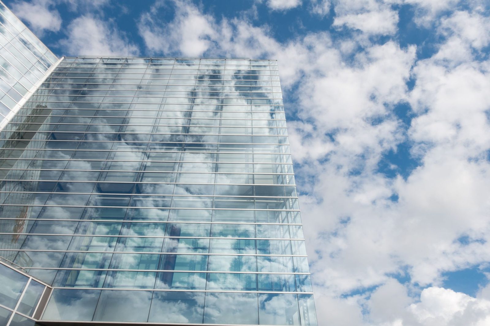 Prédio comercial com fachada de vidro transparente refletindo o céu