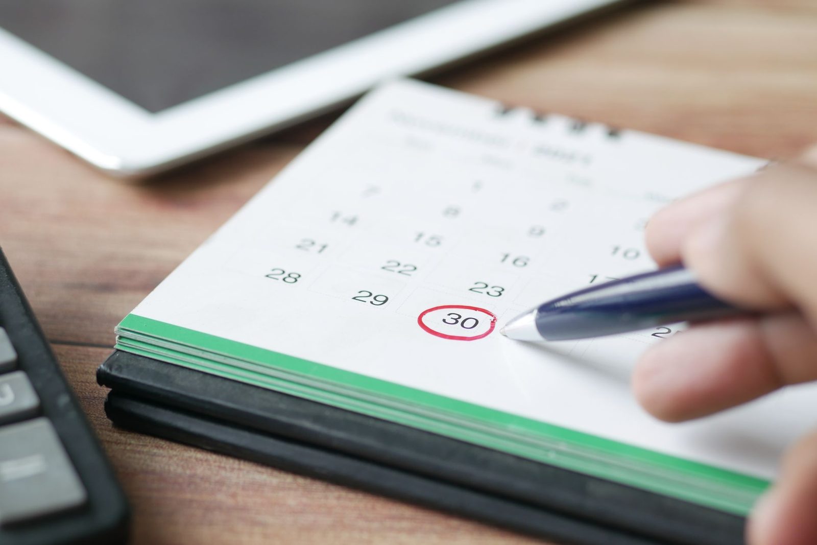 Mão marcando uma data no calendário com uma caneta, simbolizando agendamento automático
