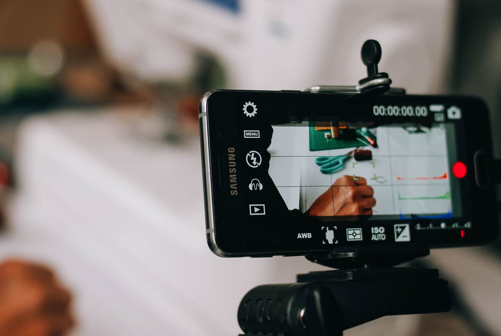 Celular preso em tripé gravando uma pessoa escrevendo em uma folha de papel