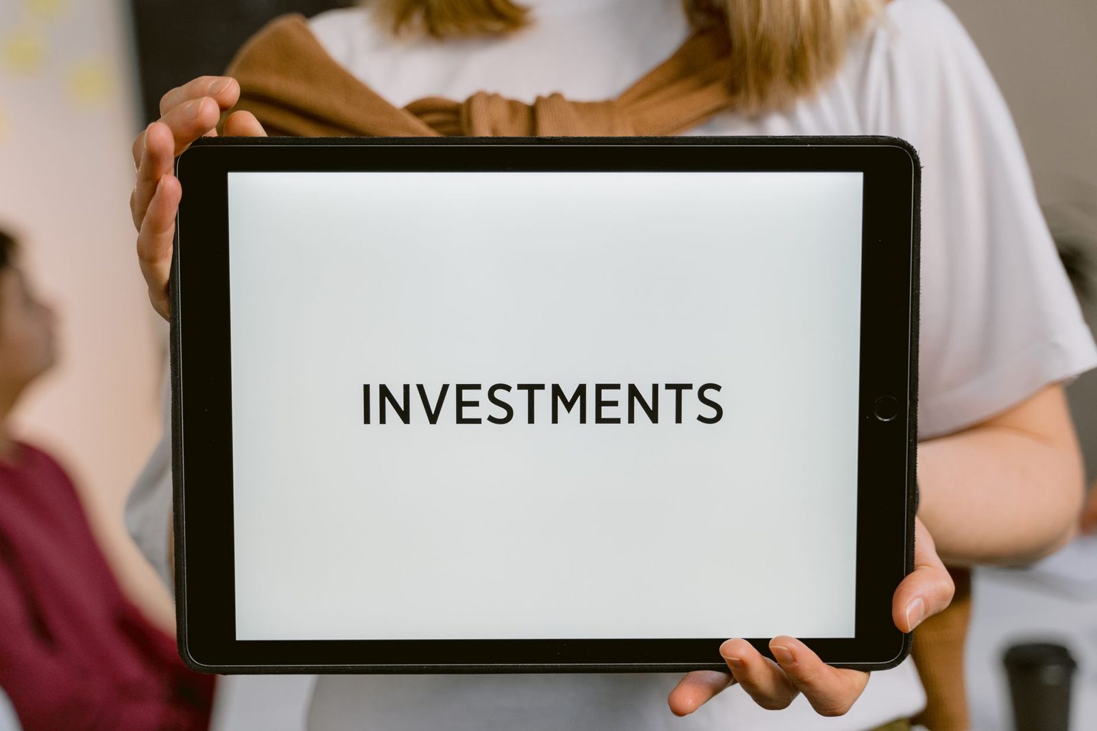 Tablet exibindo a palavra Investments segurado por uma pessoa